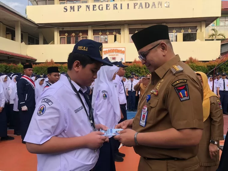 Pj Wali Kota Padang, Andree Algamar menyerahkan buku tentang pengenalan sekolah kepada salah satu siswa baru di SMPN 1 Padang.