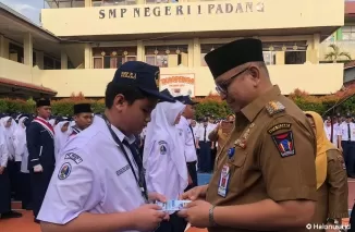 Pj Wali Kota Padang, Andree Algamar menyerahkan buku tentang pengenalan sekolah kepada salah satu siswa baru di SMPN 1 Padang.